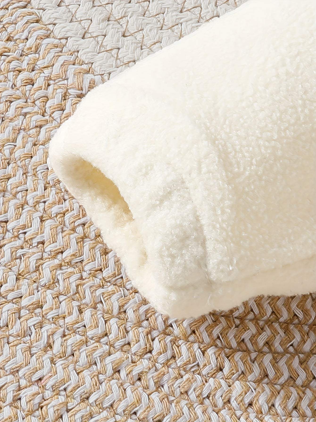 Close-up of a cozy, cream-colored baby outfit sleeve on a woven textured surface.