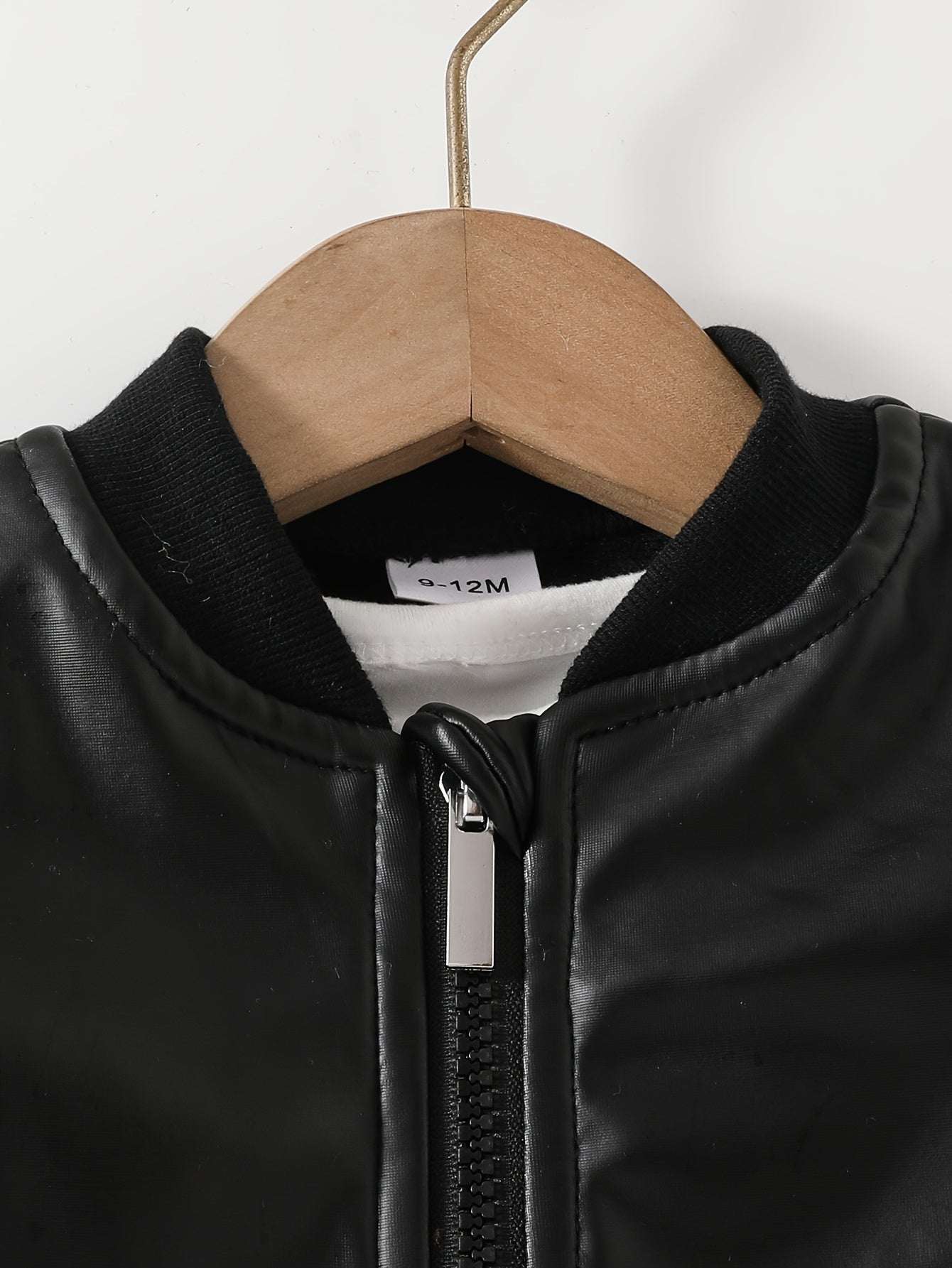 Classic black leather jacket for boys hanging on wooden hanger.