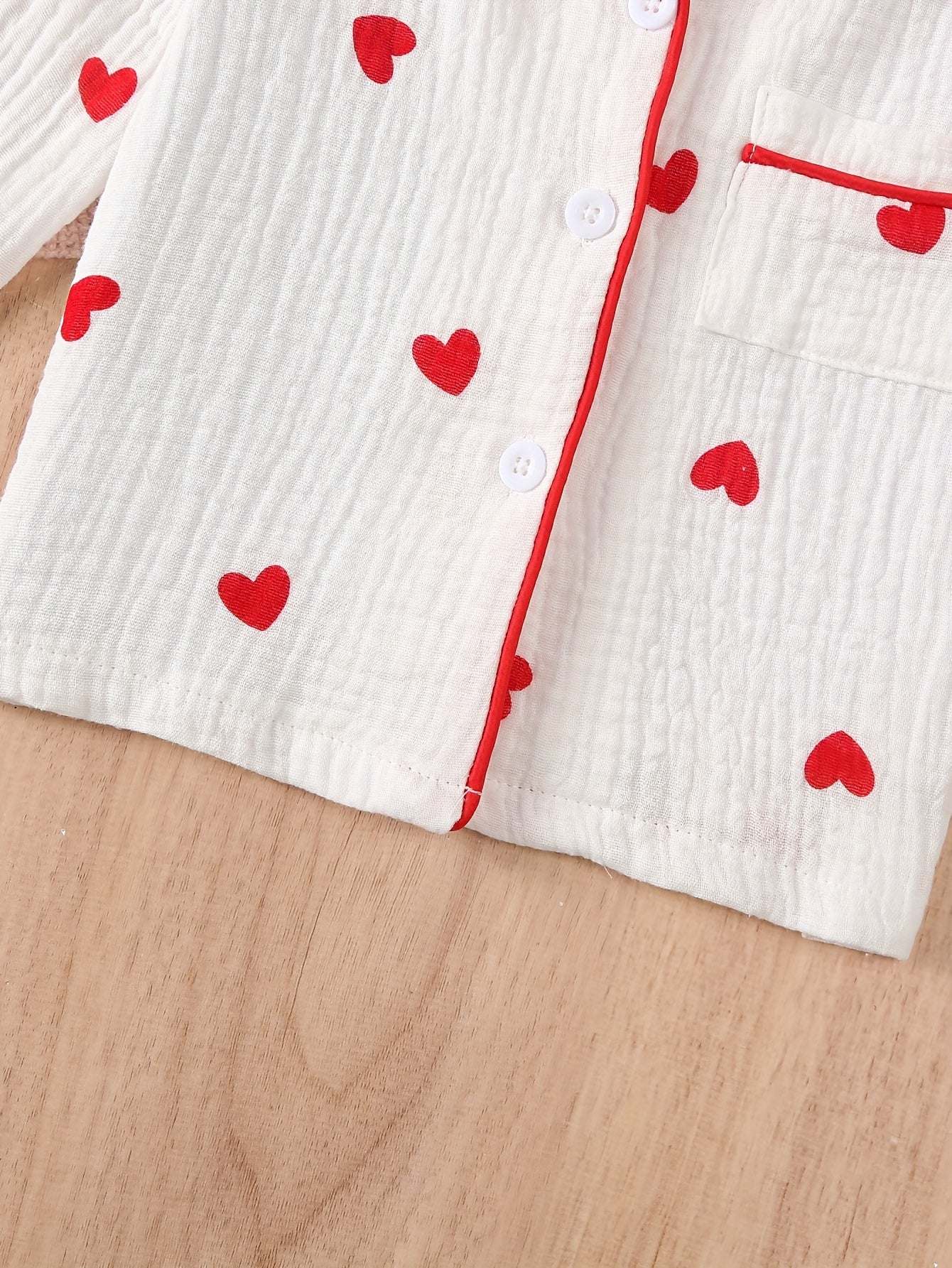 Adorable heart-patterned pajama set for girls on wooden surface.