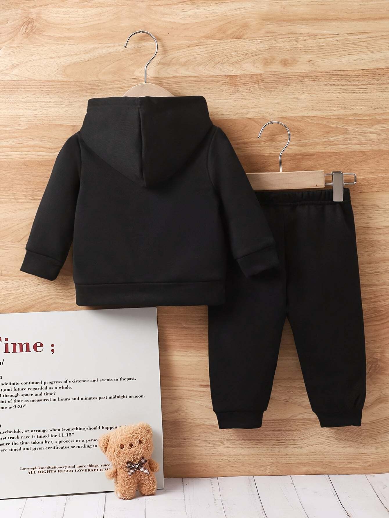 Trendy boys' black hoodie and jogger set on wooden background with teddy bear.