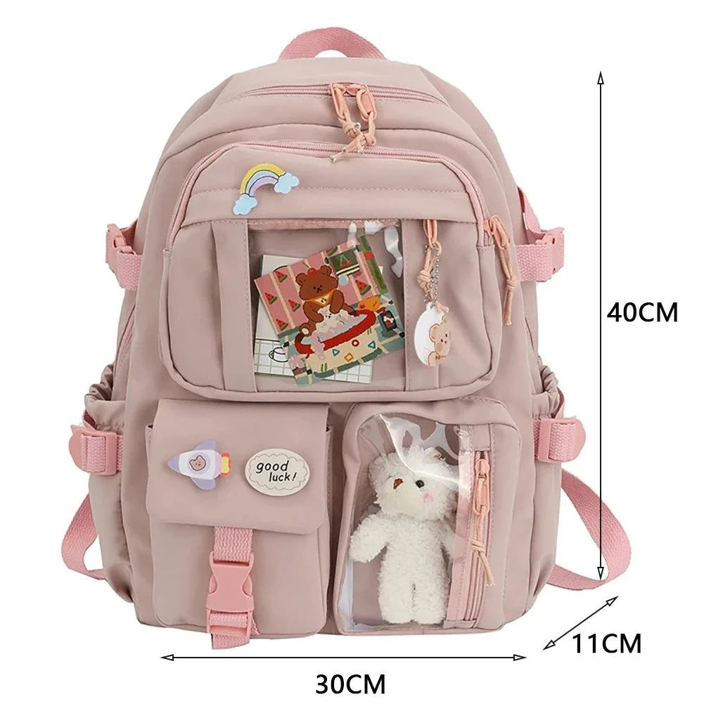 Children's schoolbag with pink design, displaying multiple compartments, plush keychain, and fun patches, ideal for school adventures.