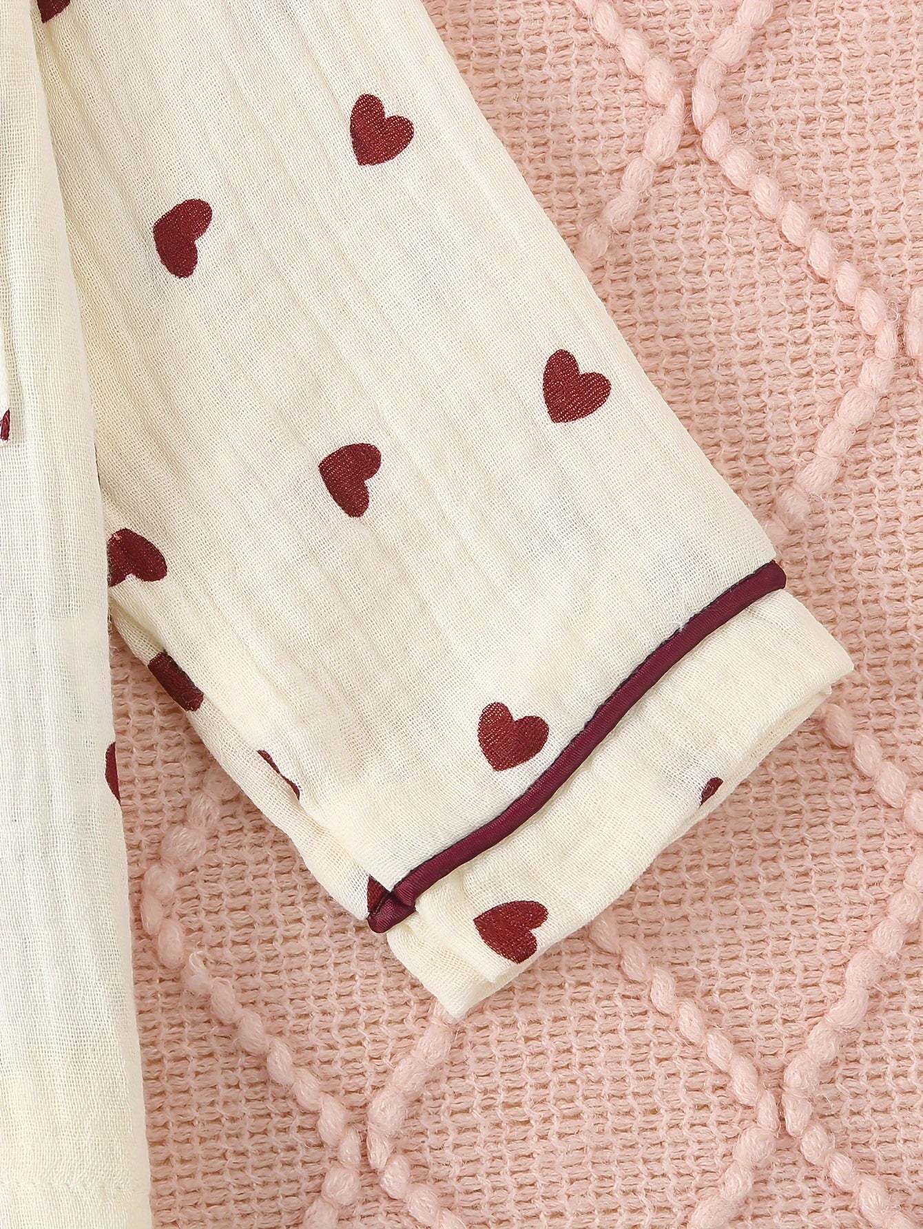 Adorable heart-patterned pajama set for girls on a pink textured background.