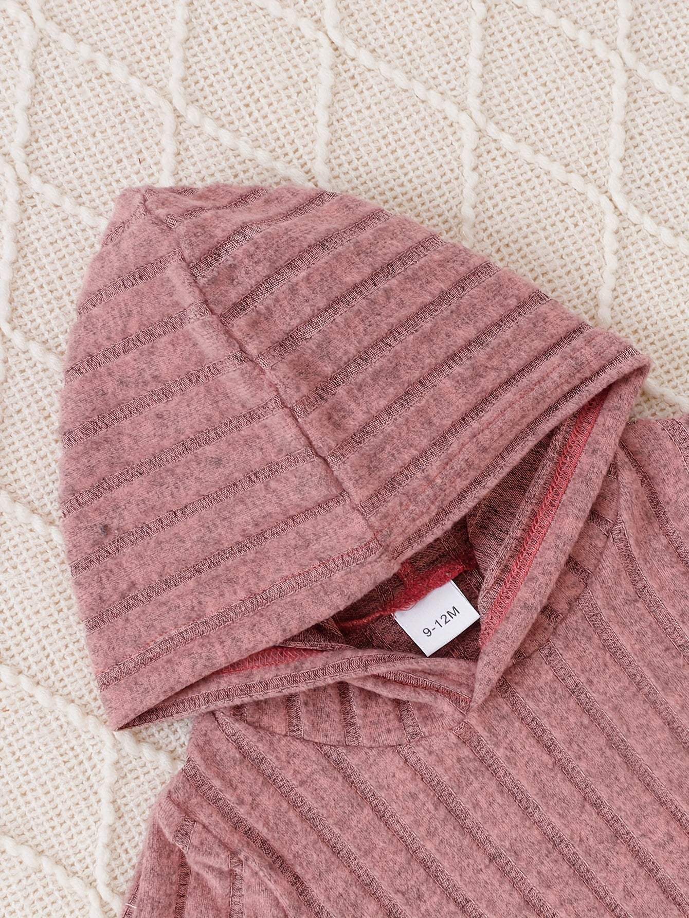 Adorable pink 2-piece shirt and pants set with a cozy hood on textured fabric.