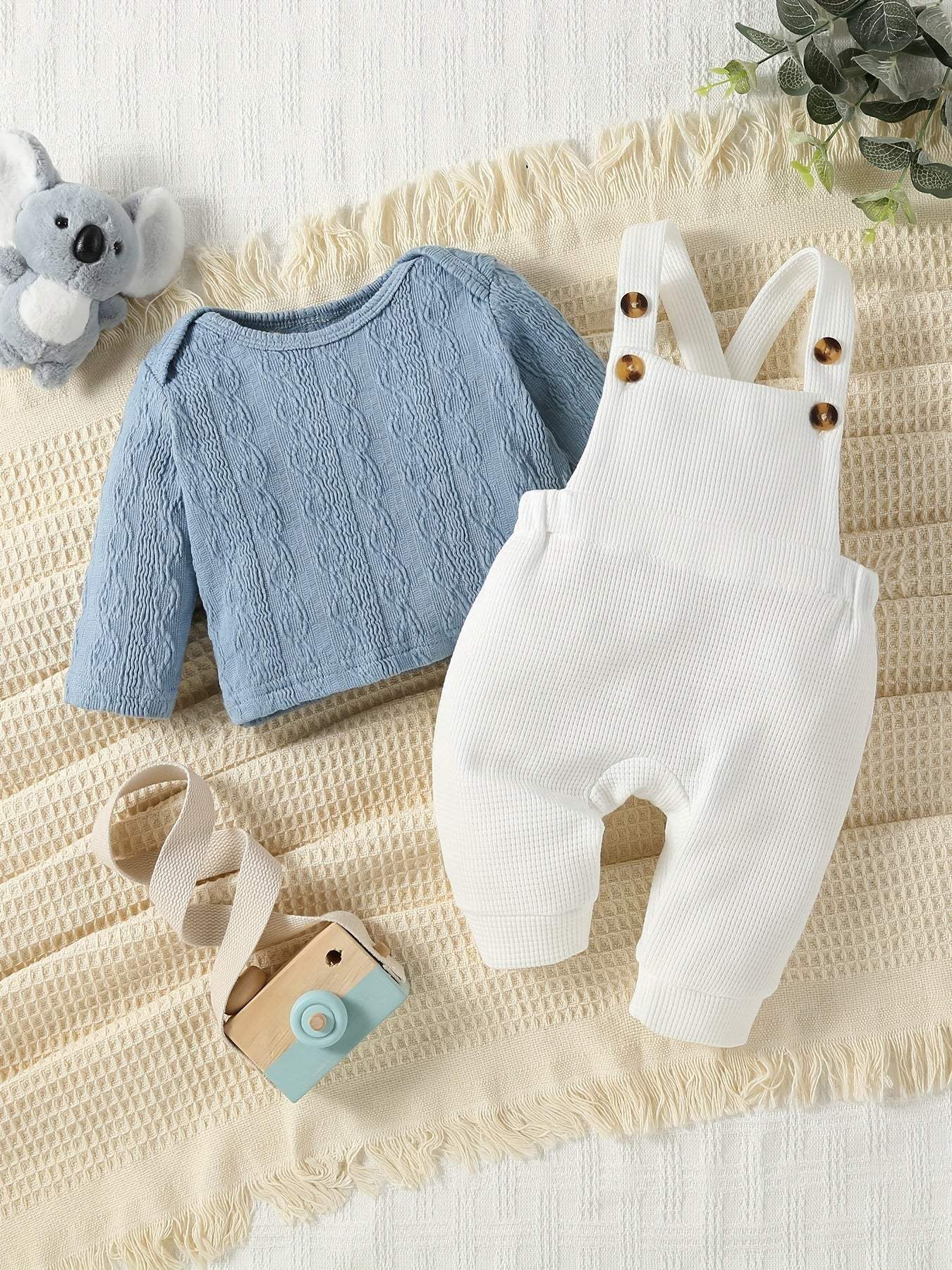 Classic 2-piece overall and shirt set for kids with blue cable-knit shirt and white overalls on a cozy beige blanket.