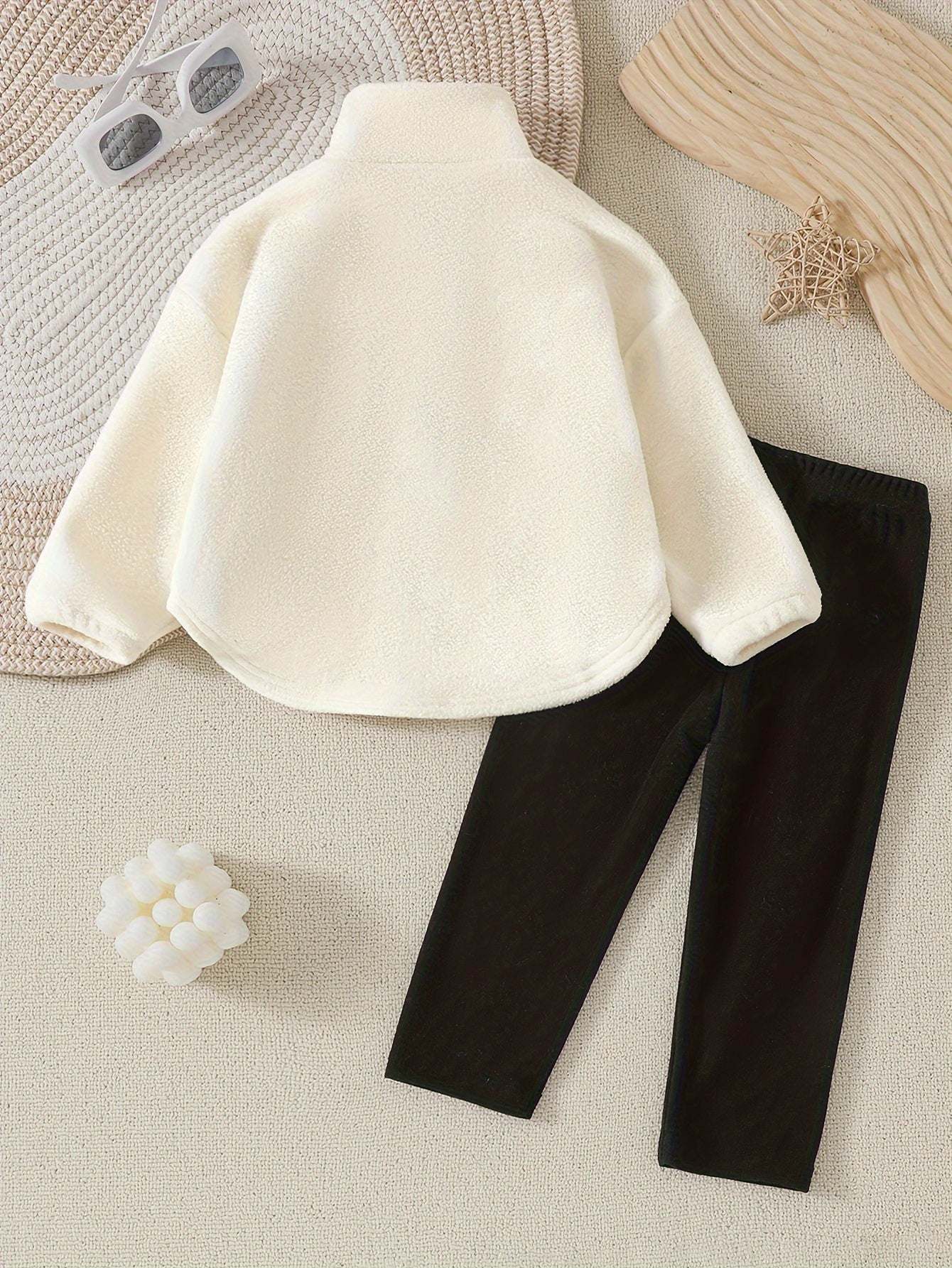 Adorable baby girl outfit set with cozy white top and black leggings on a textured surface.